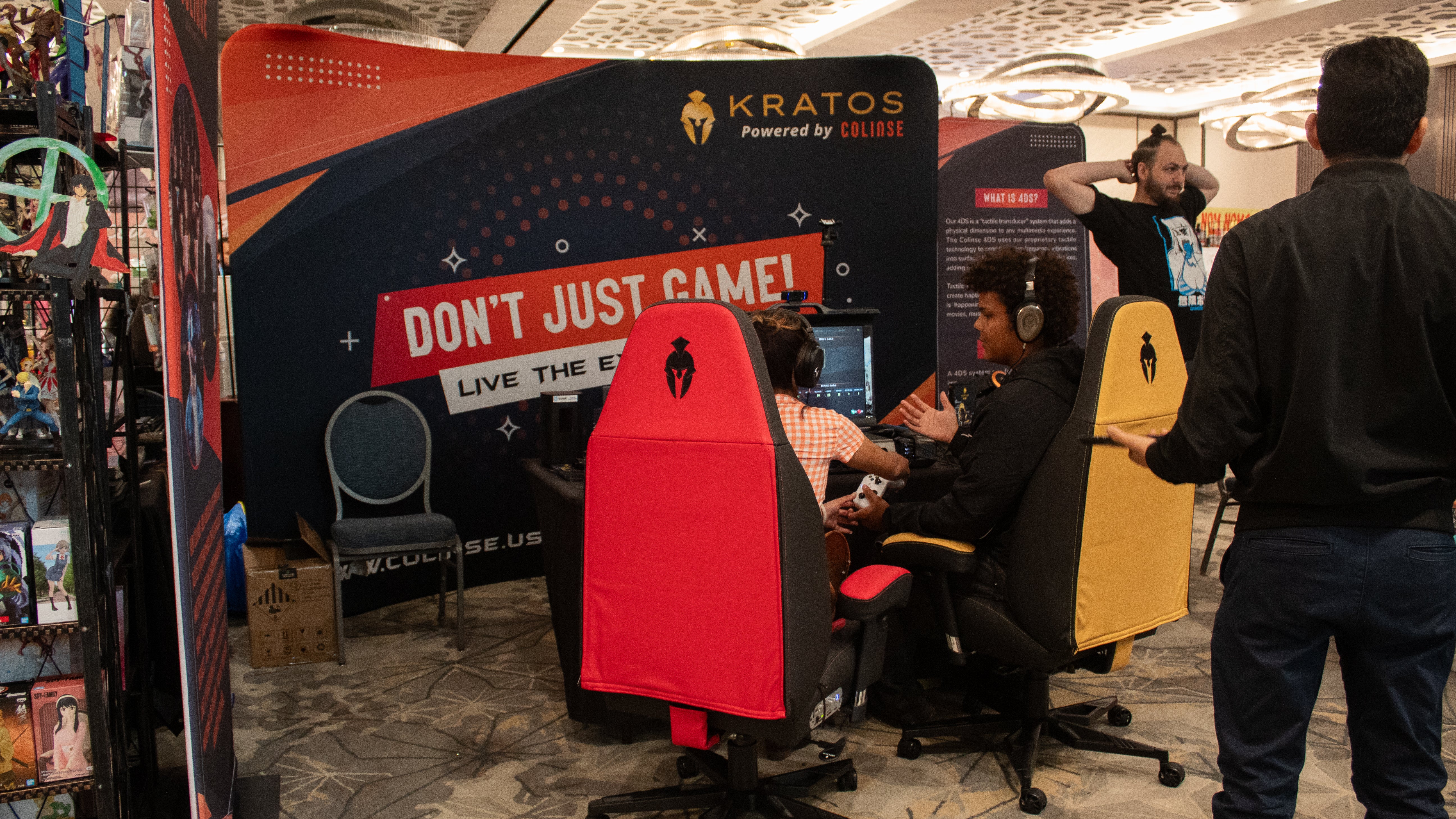 Kratos powered by Colinse booth with 3 Banners and 2 Haptic gaming chairs, one yellow and black and one black and red with 2 gamers sitting on them